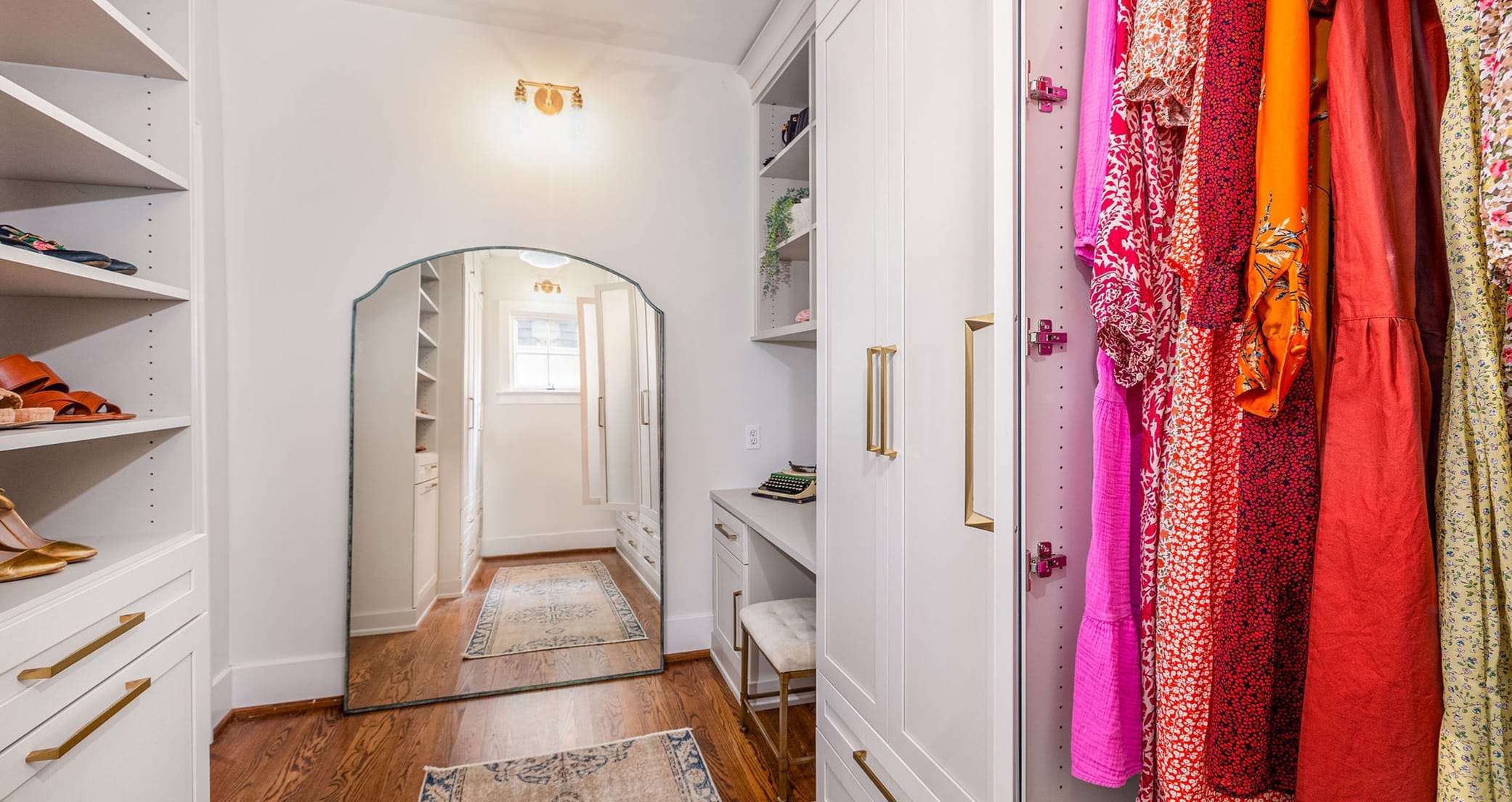 Custom walk in closet with built in open shelves, vanity and cabinets in light finish by California Closets