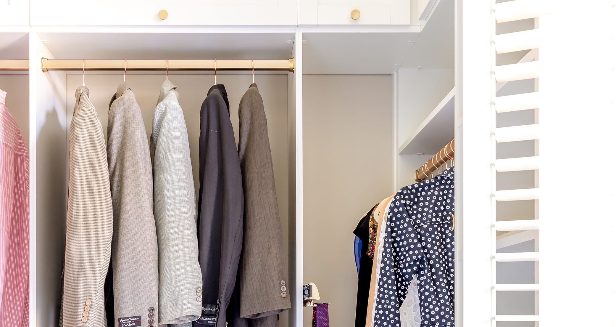 Walk in closet with organizers and rods to hold wardrobe by California Closets