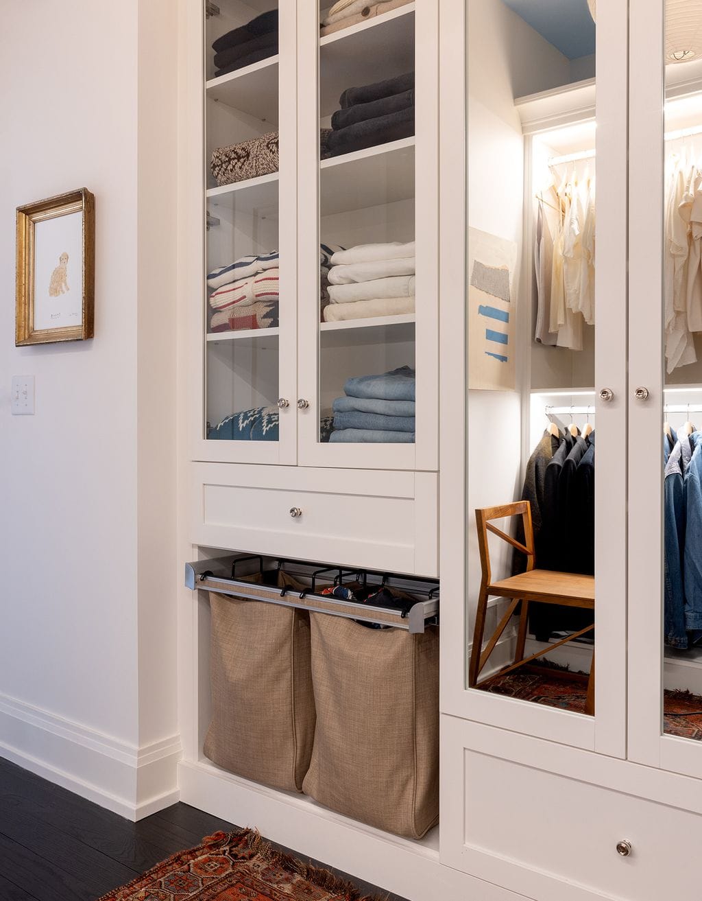 Glass cabinet doors in walk in closet design with pull out laundry hampers by California Closets