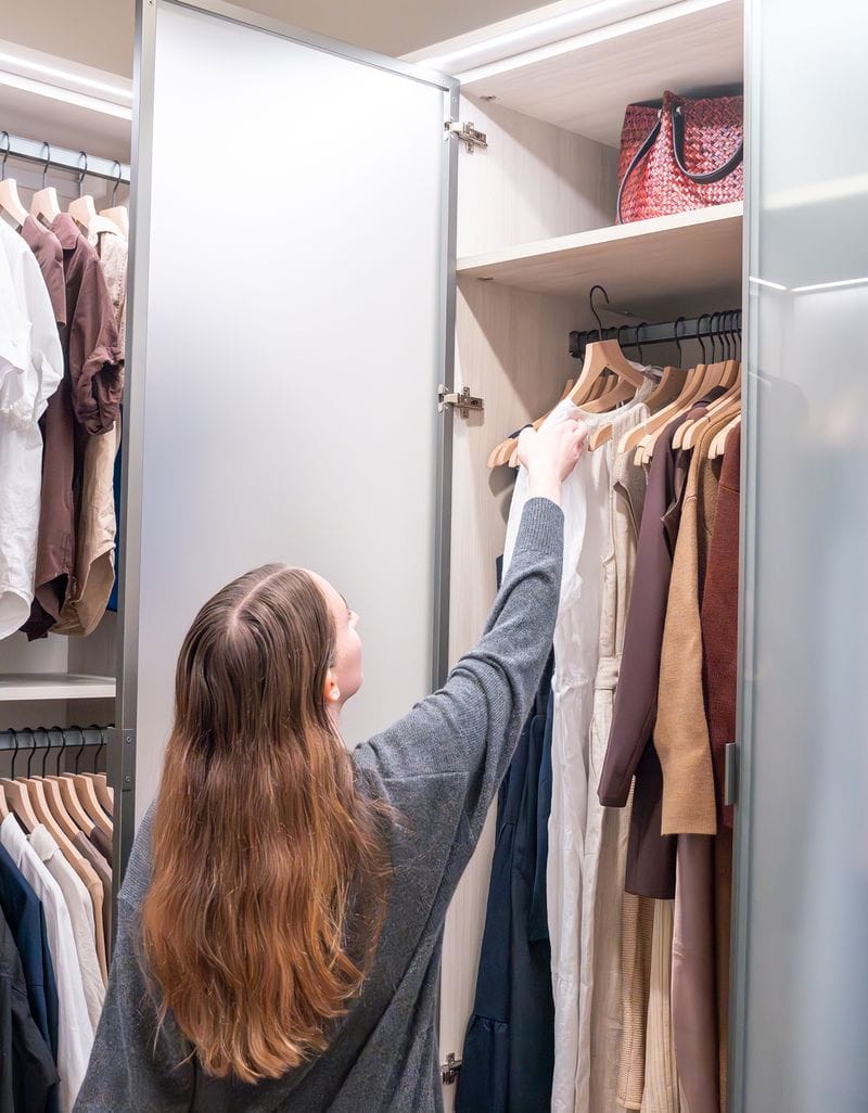 Wardrobe closet with tall hanging cabinet for long dresses in wood grain finish with glass doors created by California Closets