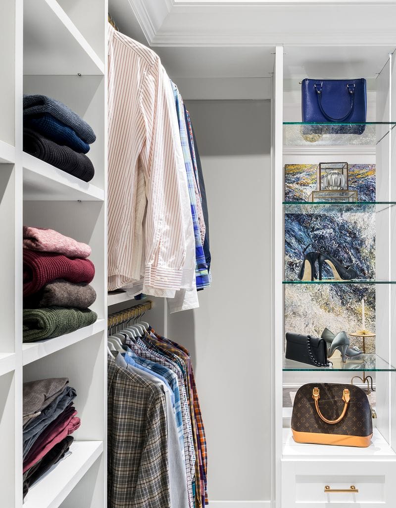 Glass shelving holds handbags, shes and accessories in a walk in closet created by California Closets
