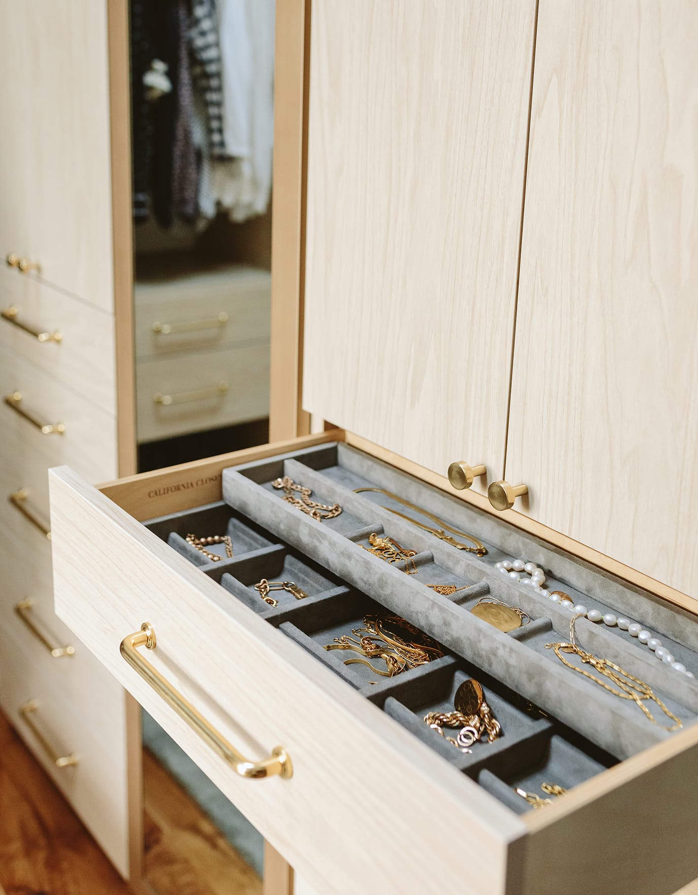 Closet drawer for jewelry and accessories with gold tone hardware and in a a light wood grain finish by California Closets