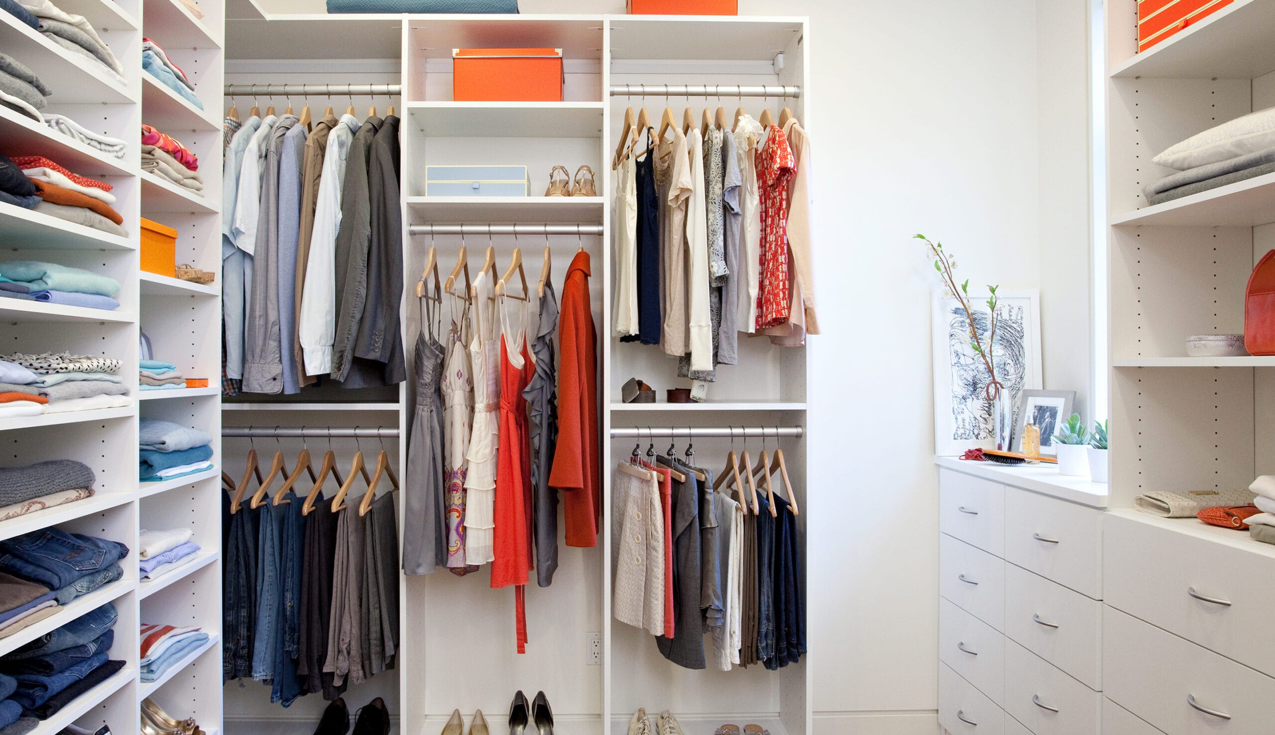 Custom-built closet with open shoe shelves, dresser drawers in white wood finish by California Closets