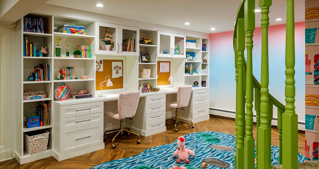 Built‑in homework station with twin desks and bookcase storage in a playroom, crafted by California Closets